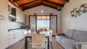 A modern kitchen with wooden cabinets, a dining area with a table and chairs, and a sofa. - 'Villetta Wild' Apartment with Sea View, Shared Terrace and Air Conditioning (Stintino)