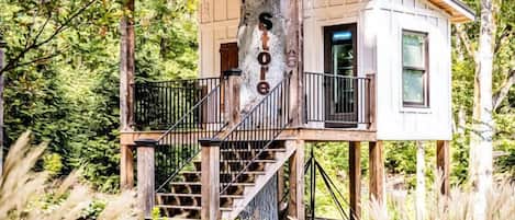 Una casa en árbol con revestimiento de madera, un balcón y una escalera que lleva a ella.