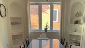 A dining room with a large rectangular table surrounded by chairs, a window with a view of a brick building, and built-in shelving on the walls.