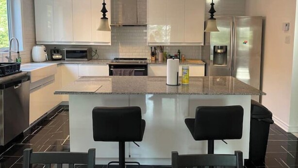 A modern kitchen with white cabinets, a central island with bar stools, stainless steel appliances, and pendant lighting.