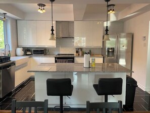 A modern kitchen with white cabinets, a central island with bar stools, stainless steel appliances, and pendant lighting. - Charming Apartment in NDG (Montréal)