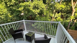 A balcony with a white railing, two wicker chairs, and a small table.