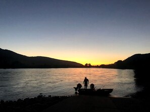 Une rivière au coucher du soleil, avec des personnes et un bateau sur la rive.