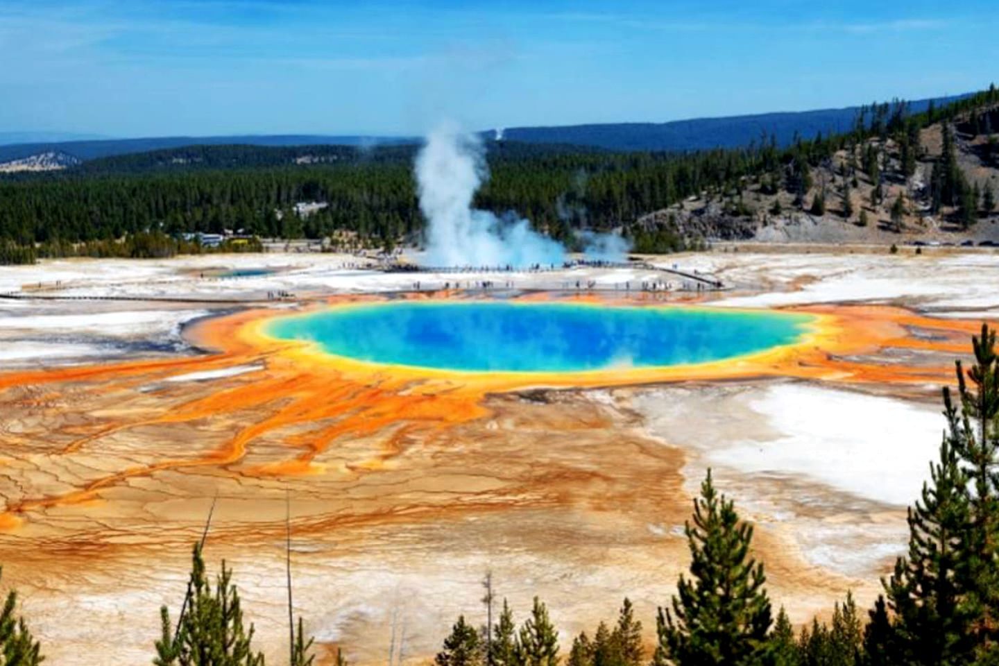 A geothermal area with a central blue pool, surrounded by orange and white terrain, and a steam vent in the background.