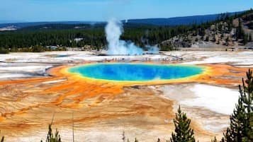 A geothermal area with a central blue pool, surrounded by orange and white terrain, and a steam vent in the background.