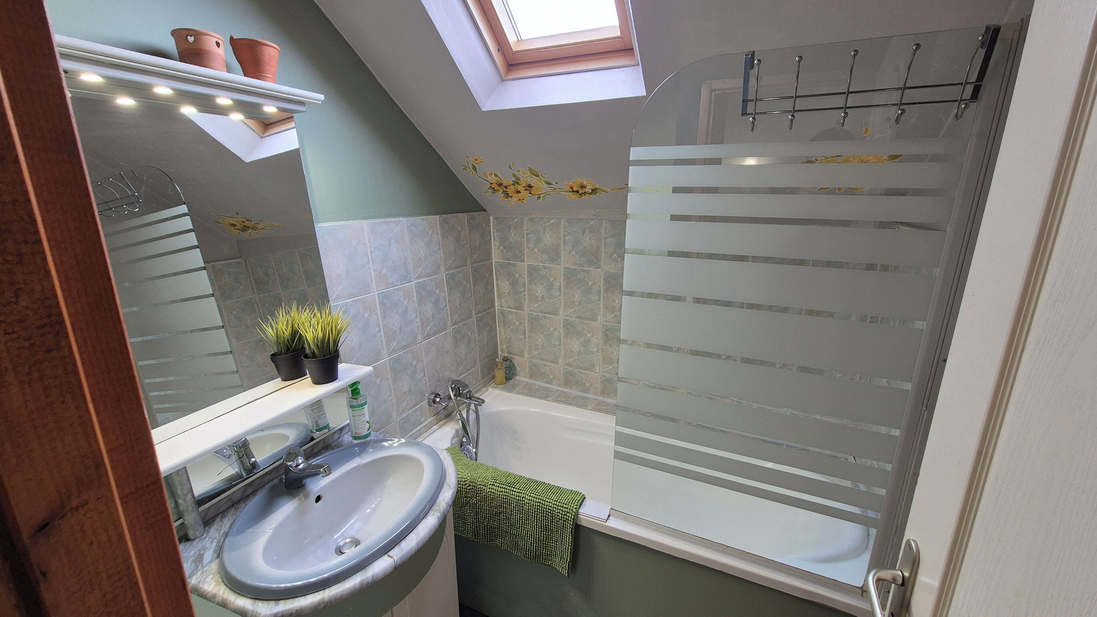 Een badkamer met dakraam, ligbad, wastafel en douche.