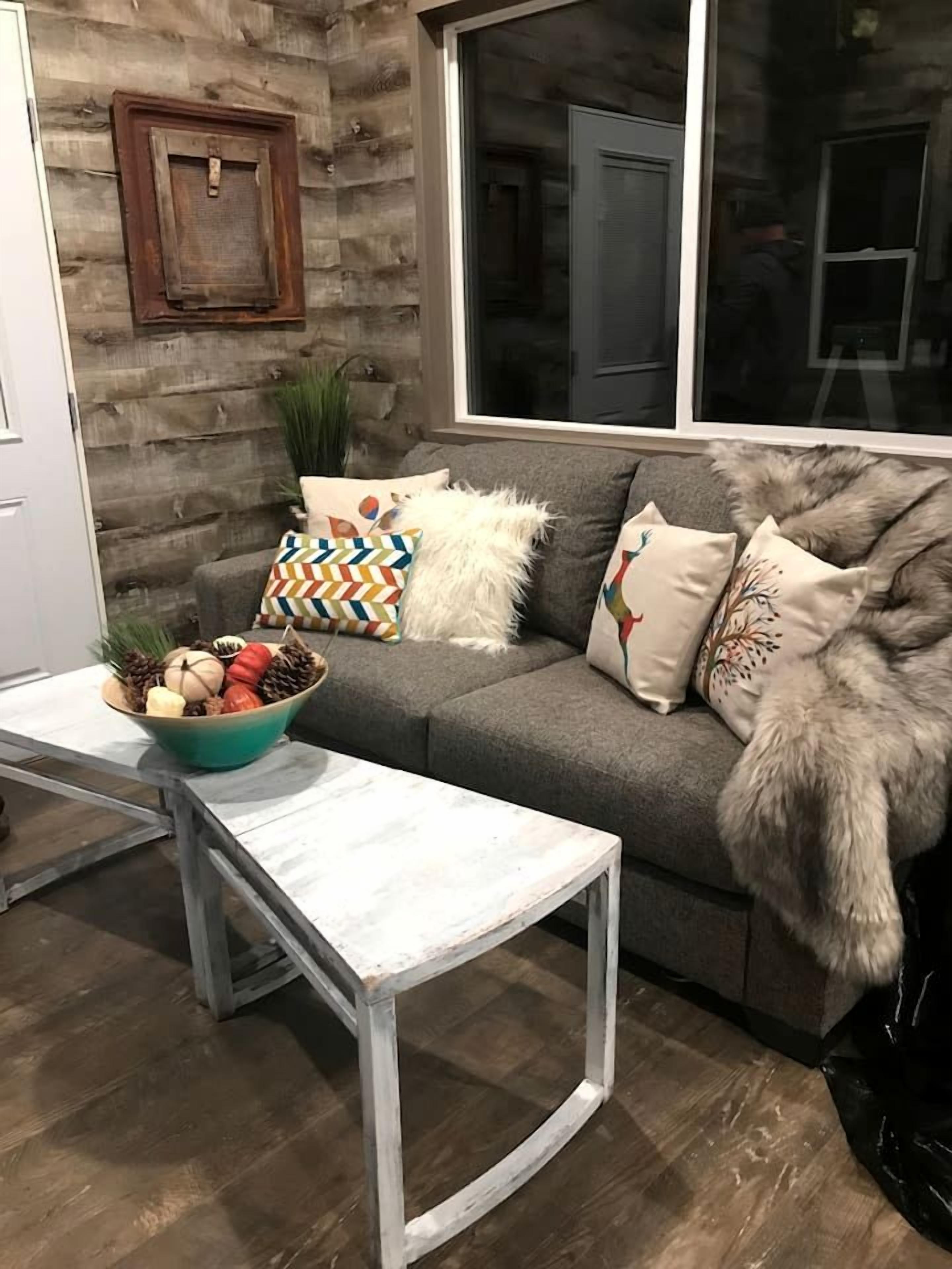 A living room with a grey sofa, white and patterned cushions, a white table, and a bowl of decorative items.