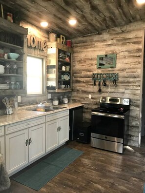A kitchen with wooden walls, a built-in sink, white cabinets, and a stainless steel oven. - Beautiful Tiny House with Wrap-Around Deck and Skylight for a Romantic Escape in Irwin, Idaho (Irwin)