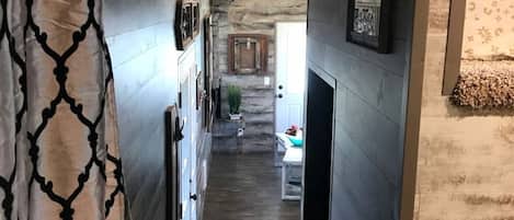 A narrow hallway with a patterned curtain, a wooden wall, and a door leading to a room with a bed.