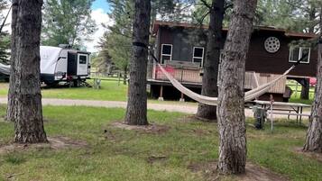 Eine Holzhütte mit einer Terrasse, einer Hängematte und einem Wohnwagen in einem Waldgebiet.