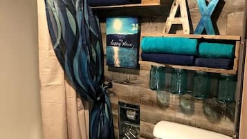 A bathroom with a shower curtain, a toilet, a shelf with folded towels, a framed picture, and wooden letters spelling 'REELAX'.