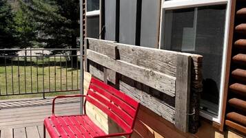 Una terraza de madera con un banco rojo, baranda metálica y vista a una montaña y árboles.