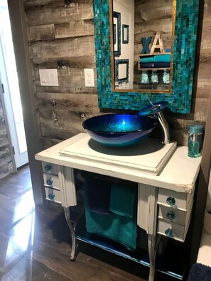 A bathroom with a wooden wall, a blue bowl sink, a mirror, and a towel rack. - Beautiful Tiny House with Wrap-Around Deck and Skylight for a Romantic Escape in Irwin, Idaho (Irwin)