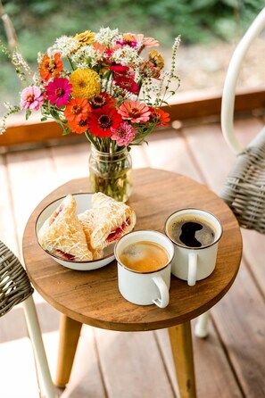 A wooden table with a floral arrangement, a plate of pastries, and two coffee mugs.