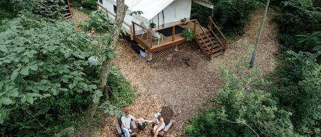 A treehouse with a deck and a fire pit, surrounded by dense forest.
