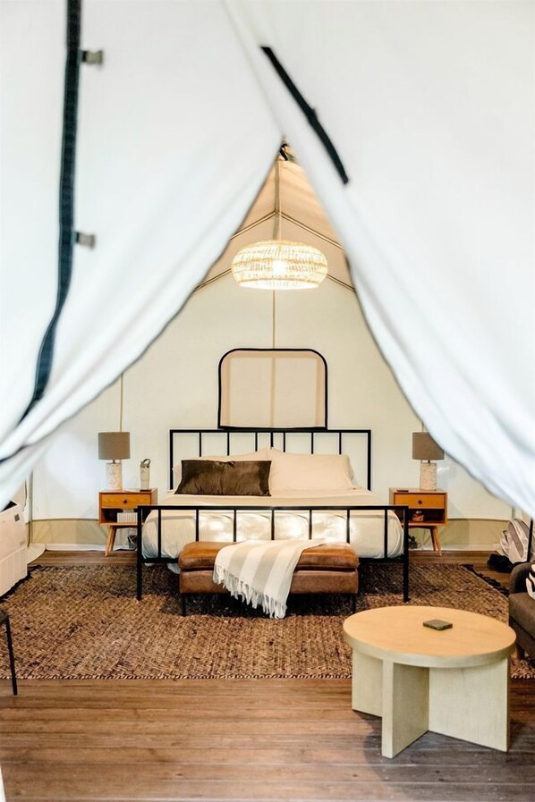 Una habitación con carpa, una cama, mesitas de noche, una mesa redonda y una lámpara colgante.