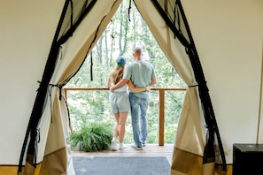 A couple standing at a wooden deck with a view of trees through a tent-like structure.