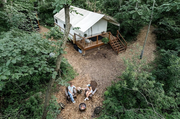 A treehouse with a deck and a fire pit, surrounded by dense forest.