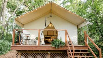 A tent-style accommodation with a wooden deck, a staircase, and a seating area with chairs.