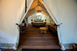 A tented accommodation with a central bed, a sofa, a round table, and a television.