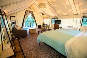 A tented accommodation room with a bed, sofa, TV, and a small table.
