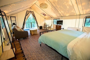A tented accommodation room with a bed, sofa, TV, and a small table.