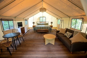 A tented accommodation with a bed, seating area, and a desk.