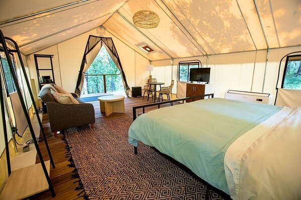 A tented accommodation room with a bed, sofa, TV, and a small table.