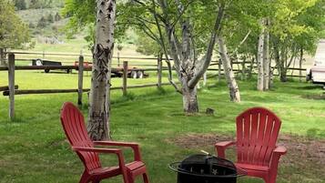 Ett grönområde utomhus med två röda Adirondack-stolar och en svart grill.