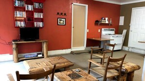 A room with a red wall, a bookshelf, a television, a wooden dining table with chairs, and a kitchen area with a stove. - Pet-Friendly Safari Tent Glamping in Swan Valley, Idaho near Jackson Hole (Irwin)