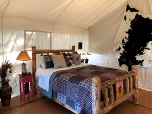 A rustic wooden bed with a checkered bedspread, a small red nightstand with a lamp, and a cowhide wall.