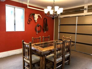 A dining area with a wooden table and chairs, a chandelier, and a red wall with a skull decoration.