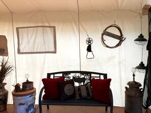 A tent interior with a black metal bench, red and patterned cushions, a star-shaped decoration, a lantern, and a metal lantern on the right.