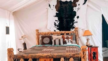 A rustic wooden bed with a wolf emblem, a white tent interior, and a mounted animal head.