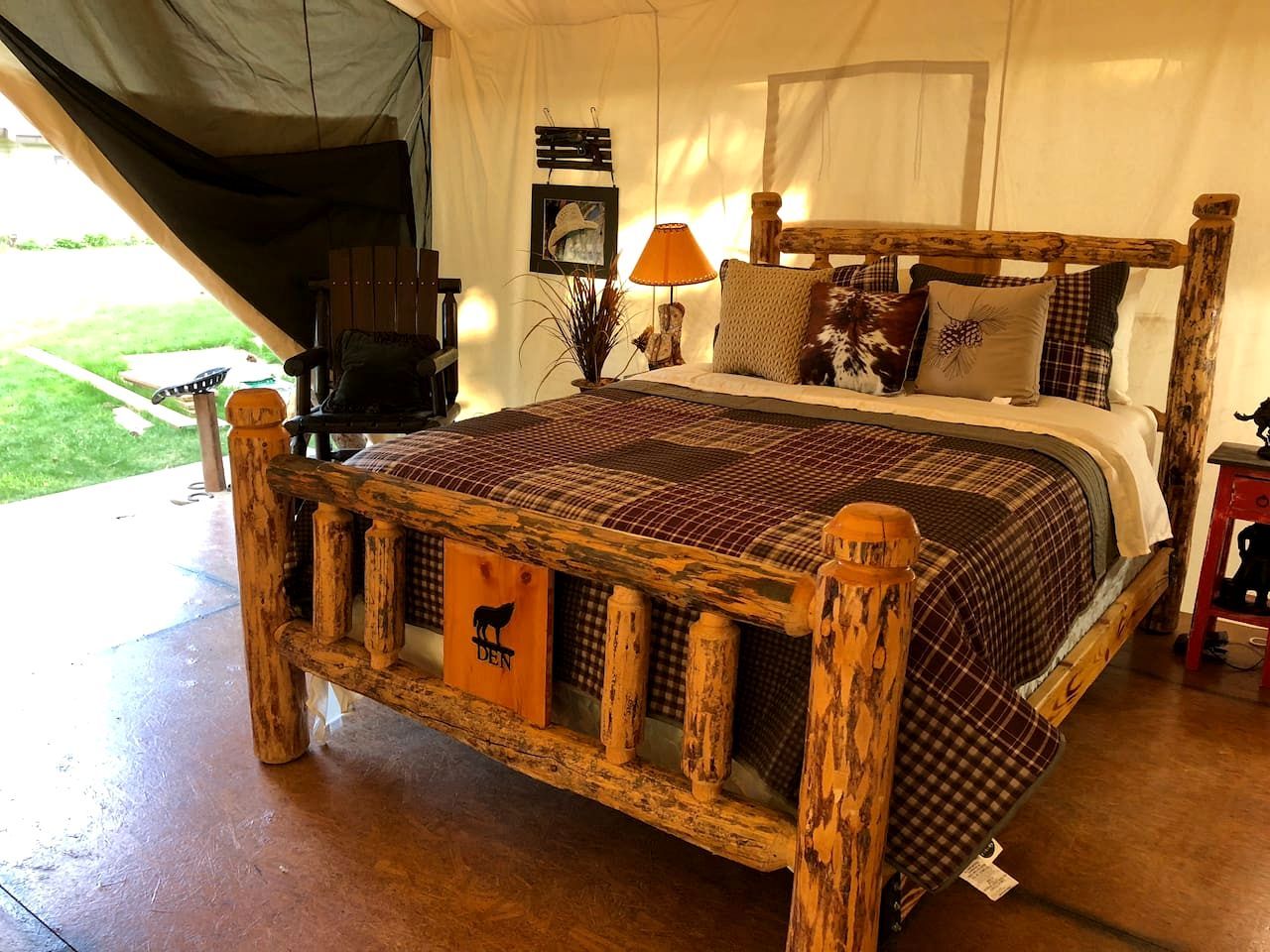 Een rustiek houten bed met een geruit beddegoed, een houten hoofdbord en een lamp op een nachtkastje.