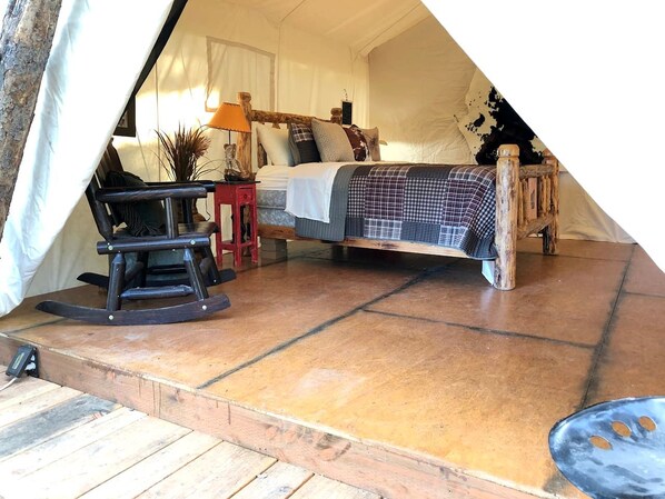 A tented accommodation with a bed, a rocking chair, a small table, and a lamp.