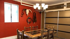 A dining area with a wooden table and chairs, a chandelier, and a red wall with a skull decoration. - Pet-Friendly Safari Tent Glamping in Swan Valley, Idaho near Jackson Hole (Irwin)