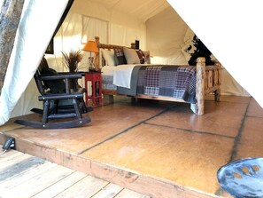 Un hébergement sous tente comprenant un lit, un fauteuil à bascule, une petite table et une lampe.