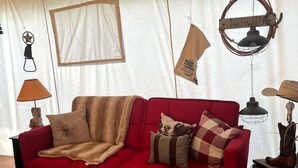 A red sofa with a blanket, a wooden coffee table, and a hanging lamp. - Pet-Friendly Safari Tent Glamping in Swan Valley, Idaho near Jackson Hole (Irwin)