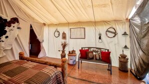 A tent interior with a bed, bench, hanging lanterns, and a framed picture on the wall. - Pet-Friendly Safari Tent Glamping in Swan Valley, Idaho near Jackson Hole (Irwin)