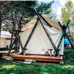 Ein teepee-ähnliches Zelt mit einer Holzplattform und einem kleinen Tisch mit einem Teddybären.