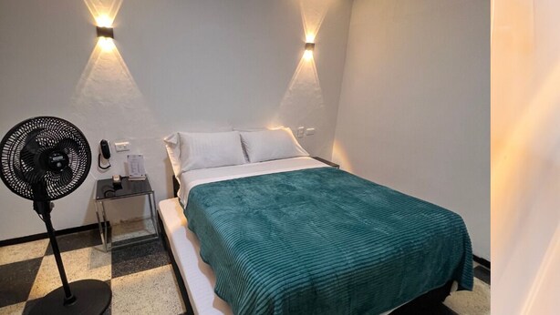 A hotel room with a bed, a nightstand, a fan, and two wall-mounted lights. - Hotel Ensueño (Pereira)