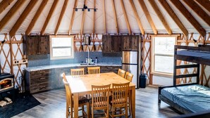 Un intérieur chaleureux avec une table à manger en bois, des chaises, un coin cuisine et un lit superposé.