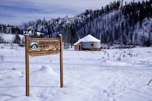 A wooden sign for Idaho Wilderness Yurts with a yurt in the background.