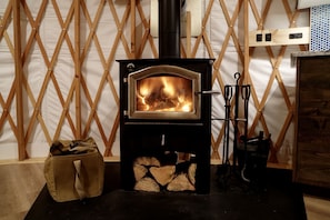 A wood-burning stove with a fire, a bag of wood, and a metal rack.