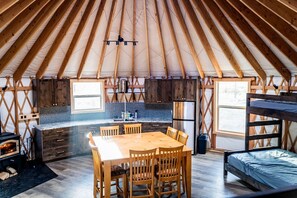 Un intérieur chaleureux avec une table à manger en bois, des chaises, un coin cuisine et un lit superposé.