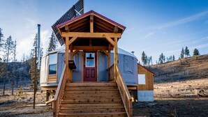 Une cabane en bois avec une porte rouge, un escalier menant à l’entrée et un panneau solaire sur le toit.