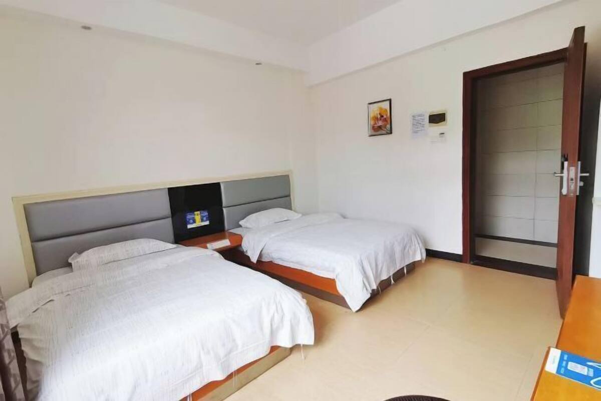 Hotellihuone, jossa on kaksi erillistä sänkyä, puinen työpöytä, pieni televisio ja lasipaneelilla varustettu ovi.