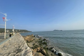 Une promenade en bord de mer, avec un muret en pierre, un ciel dégagé et une mer calme.