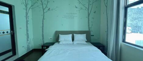 A bedroom with a bed, a nightstand, a window, and a wall with tree decals.